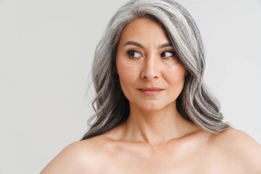 Beyaz arka planda yalnız bırakılmış, gri saçlı, olgun, üstsüz bir kadın.