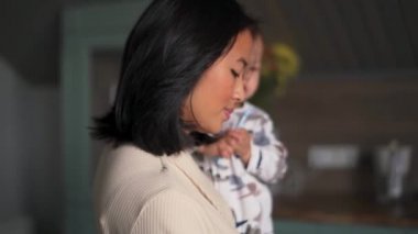 Neşeli Asyalı anne mutfakta bebeği kollarında sallıyor.