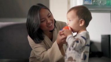 Asyalı anne bebeğe mutfakta domates yediriyor.