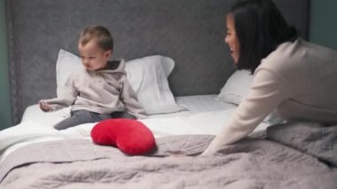 Asyalı anne oğluyla yatakta yastık oyunu oynuyor.