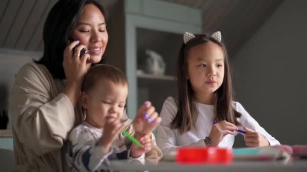 Uśmiechnięta Azjatka Rozmawia Przez Telefon Opiekuje Się Dziećmi Kuchni — Wideo stockowe
