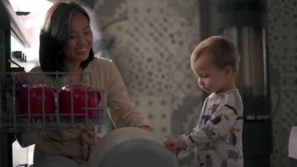 Asiático Positivo Hijo Cerrando Lavavajillas Con Platos Lado Mamá — Vídeo de stock