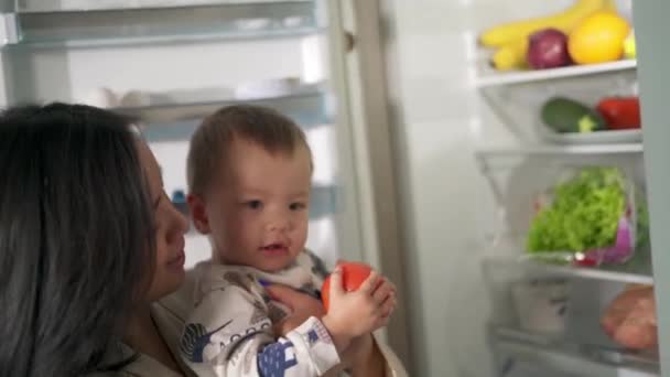 亚洲妈妈抱着孩子 从冰箱里拿出一个西红柿 — 图库视频影像