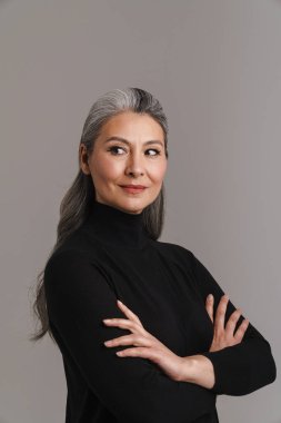 Olgun Asyalı beyaz saçlı kadın kollarını kavuşturup gri arka planda izole bir şekilde poz veriyor.