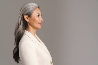 Beyaz saçlı, olgun Asyalı bir kadın. Gri arka planda tek başına poz veriyor.