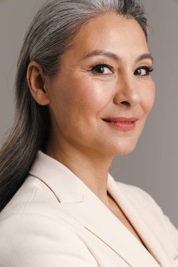 Beyaz saçlı, gülümseyen ve gri arka planda izole edilmiş kameraya bakan olgun bir kadın.