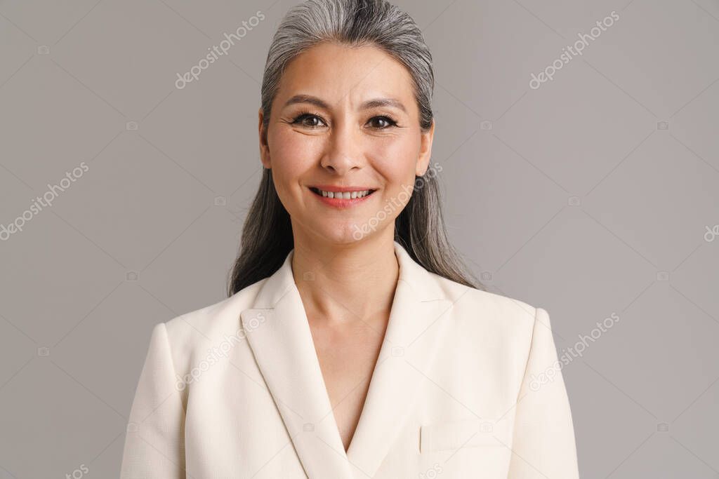 Mature woman with white hair smiling and looking at camera isolated over grey background
