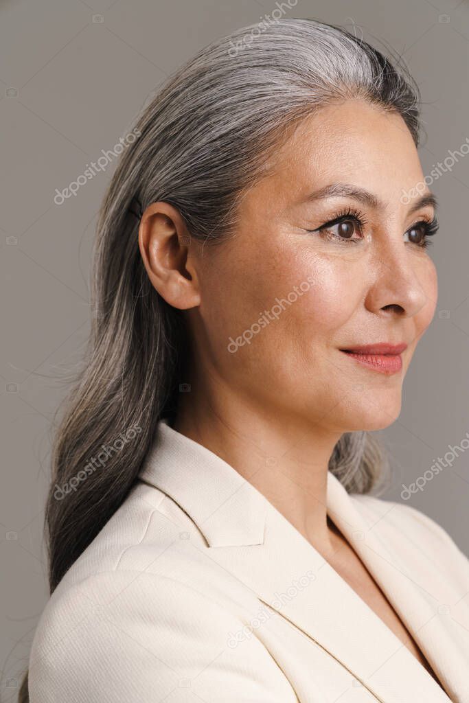 Mature woman with white hair posing and looking aside isolated over grey background