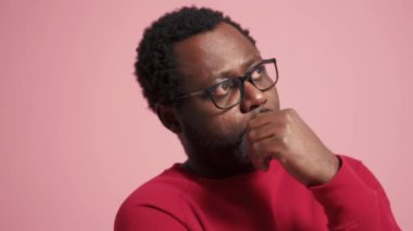 Meditasyon yapan yetişkin Afrikalı adam pembe stüdyoda yan tarafa bakıyor.