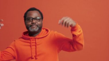 Olgun Afrikalı adam turuncu stüdyoda dans ediyor.