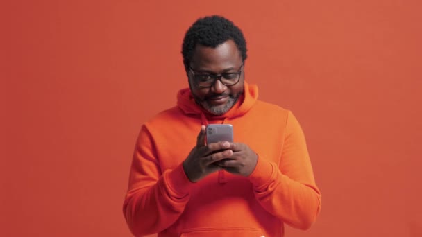 Lächelnder Älterer Afrikanischer Mann Tippt Orangefarbenen Studio Telefon — Stockvideo