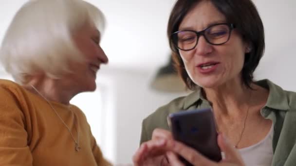 笑中年妇女在家里沙发上聊天和看手机 — 图库视频影像