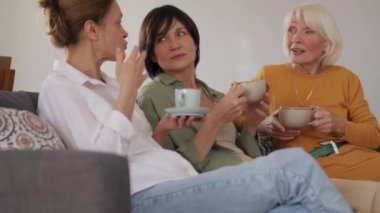 Olumlu olgun kadınlar evde çay içip sohbet ediyorlar.