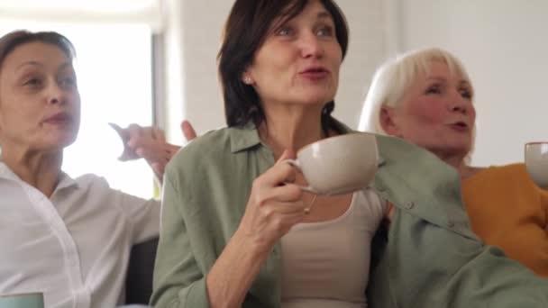 笑顔成熟した女性見ますテレビと飲み物茶に家 — ストック動画