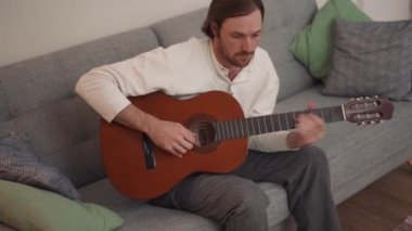 Kendine güvenen, uzun saçlı bir adam gitar çalmayı evde aldığı bir video dersinden öğreniyor.