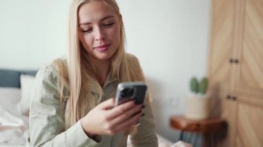 Gülümseyen sarışın kadın evde telefonla mesaj atıyor.