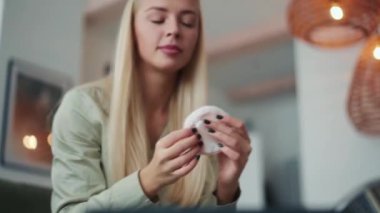 Gülümseyen sarışın kadın evde bir süngerle yüzünü pudralıyor.