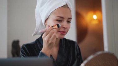 Kafasında havluyla evde makyaj yapan mutlu bir kadın.