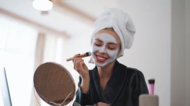 Kafasında havluyla gülen kadın evde maske takıyor.