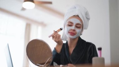 Kafasında havluyla evde maske takan pozitif sarışın bir kadın.