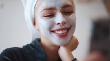 Kafasında havluyla evde telefona bakan dalgın sarışın kadın.