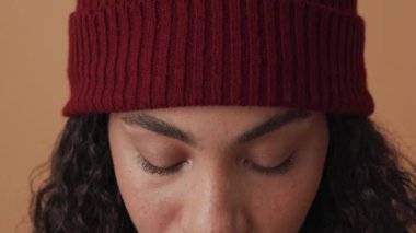 Mutlu Afrikalı kıvırcık saçlı kadın bej stüdyoda kameraya bakıyor.