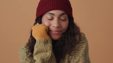 Bej renkli stüdyoda kameraya poz veren Afrikalı kıvırcık saçlı kadın.