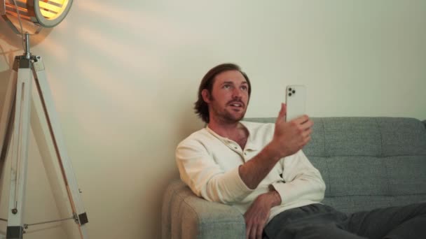 Schöner Langhaariger Mann Telefoniert Videoanruf Während Hause Auf Dem Sofa — Stockvideo