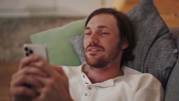 Ciddi Uzun Saçlı Bir Adam Evdeki Kanepede Yatarken Telefona Bakıyor — Stok video