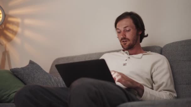 Seriöser Langhaariger Mann Der Hause Auf Dem Sofa Laptop Arbeitet — Stockvideo