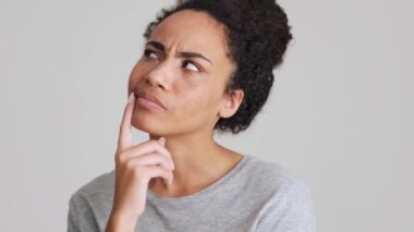 Gri tişörtlü Afrikalı kadın gri stüdyoda bir şey düşünüyor.