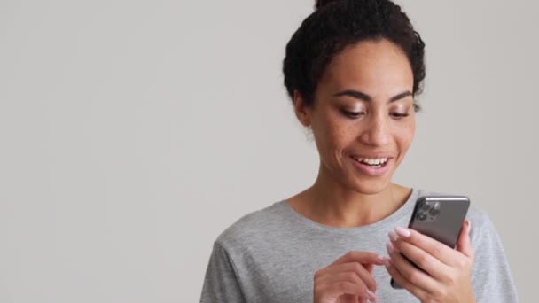 Mujer Africana Sonriente Camiseta Hojeando Cinta Por Teléfono Estudio Gris — Vídeo de stock