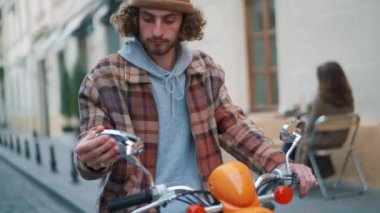 Yoğunlaşmış kıvırcık saçlı adam sokakta bir motosikletin aynasına bakıyor.