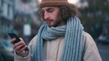 Açık havada telefonla mesajlaşan mutlu kıvırcık saçlı adam.