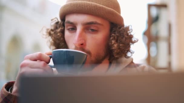 自信を持って中髪の男はノートパソコンを見て 屋外のカフェでコーヒーを飲む — ストック動画