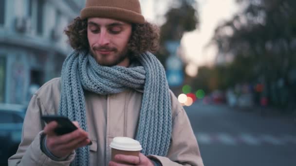 Vrolijke Krullende Man Sms Telefoon Met Beker Zijn Handen Buiten — Stockvideo