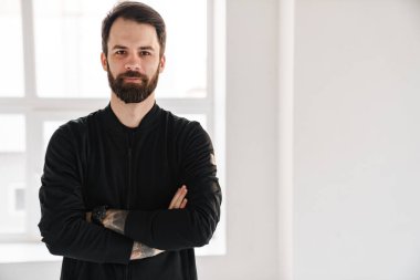 Sakin, esmer, beyaz bir adam spor kıyafetleri içinde kollarını kavuşturmuş bekliyor.