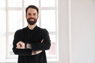 Gülümseyen esmer, beyaz bir adam spor giyim kuşamında evde dikilip akıllı bakışlara bakıyor.