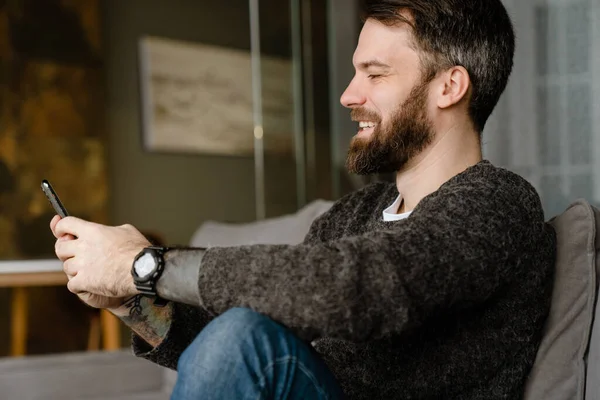 Bearded Man Using Mobile Phone Smiling While Sitting Sofa Home — Stock Photo, Image