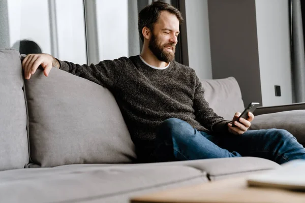 Barbudo Hombre Europeo Usando Teléfono Móvil Mientras Está Sentado Sofá — Foto de Stock