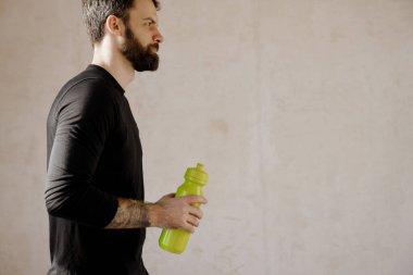 Orta yaşlı, sakallı, elinde su şişesi olan beyaz bir adam.