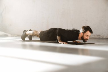 Kendine güvenen orta yaşlı beyaz sporcu, parlak bir oda tahtasında egzersiz yapıyor.