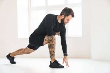 Kendine güvenen orta yaşlı beyaz sporcu, parlak bir odada egzersiz yapıyor.