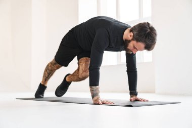 Kendine güvenen orta yaşlı beyaz sporcu, parlak bir odada egzersiz yapıyor.