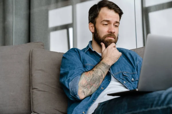 Homem Europeu Barbudo Trabalhando Com Laptop Enquanto Sentado Sofá Casa — Fotografia de Stock