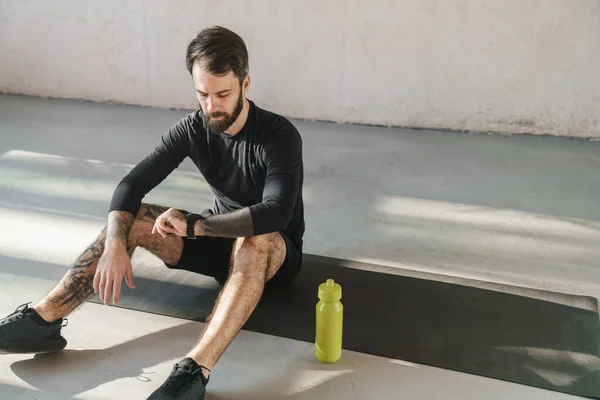 Jovem Morena Barbuda Desportista Sentado Tapete Fitness Dentro Casa Olhando — Fotografia de Stock