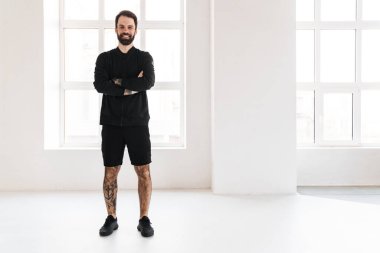 Gülümseyen esmer, beyaz bir adam spor giyim kuşamında evde dikiliyor.