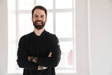 Gülümseyen esmer, beyaz bir adam spor giyim kuşamında evde dikiliyor.