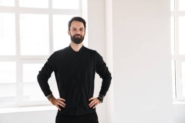 Sakin, esmer, beyaz bir adam spor giyim kuşamında içeride dikiliyor.