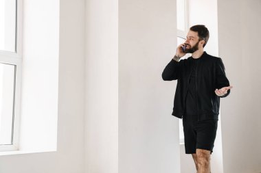 Gülümseyen esmer, beyaz bir adam spor giyim kuşamında içeride cep telefonuyla konuşuyor.